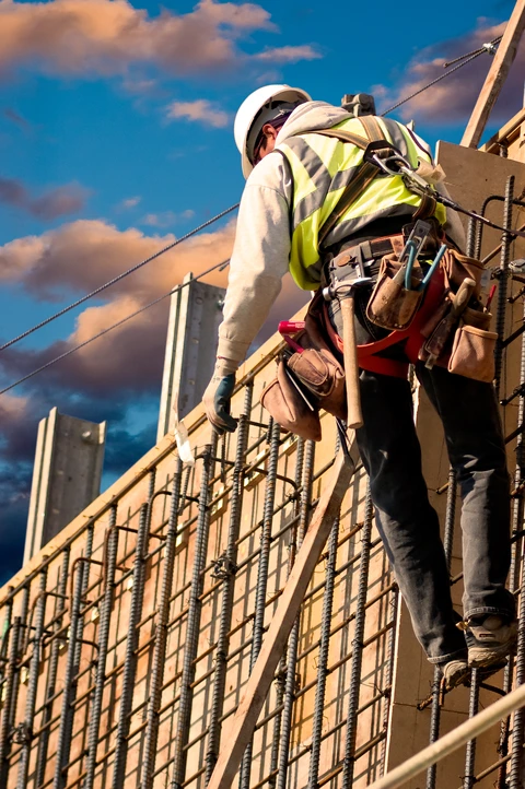 Chantier de construction extérieur, ouvrier du bâtiment équipé d'un harnais de sécurité travaillant sur structure en béton armé avec coffrage
