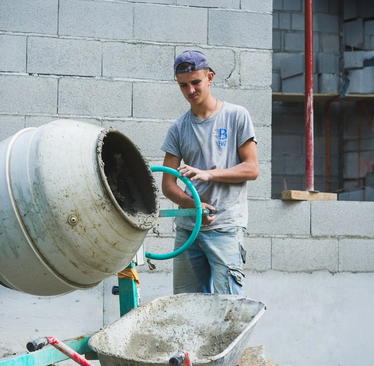 Chantier de construction en extérieur avec ouvrier appliquant mortier entre blocs de béton cellulaire pour édification d'un mur