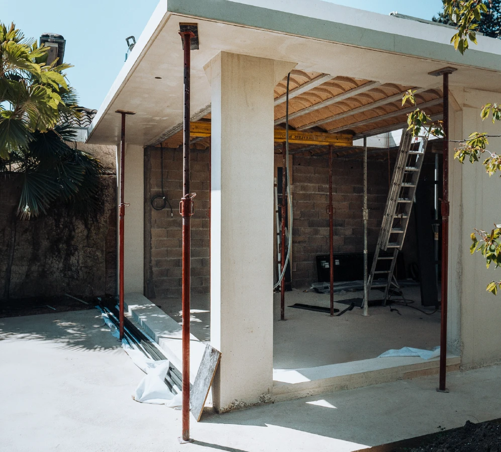 Maison individuelle contemporaine, vue extérieure, façade enduite gris clair, toiture en tuiles canal terre cuite avec panneaux photovoltaïques
