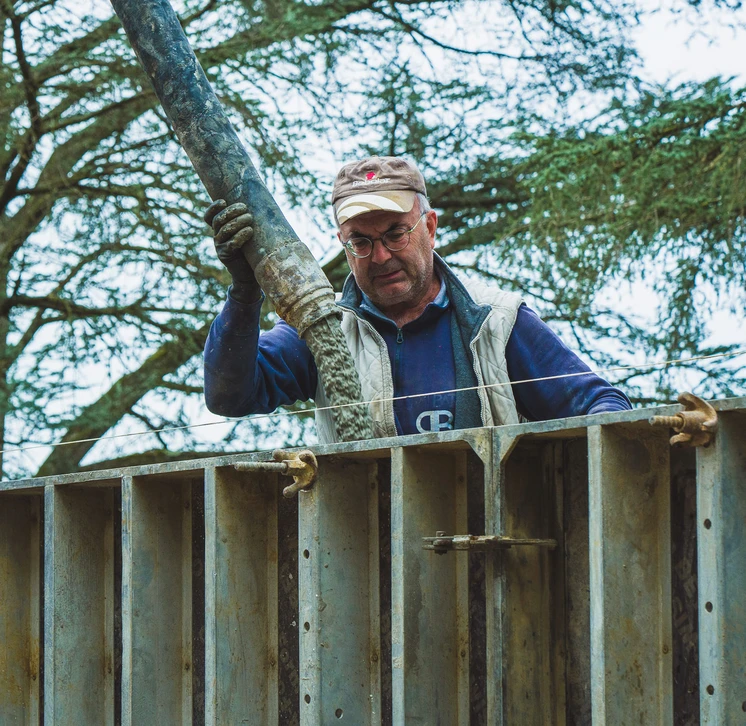 Photographie d'un chantier de construction neuve montrant un ouvrier maçon en train de poser des parpaings ou de construire une structure murale en gros œuvre, avec des matériaux de chantier visibles (parpaings, mortier, niveau, outils maçonnerie), dans un environnement de chantier professionnel et organisé. L'image doit clairement illustrer les travaux de gros œuvre et de structure, pas de finition.
