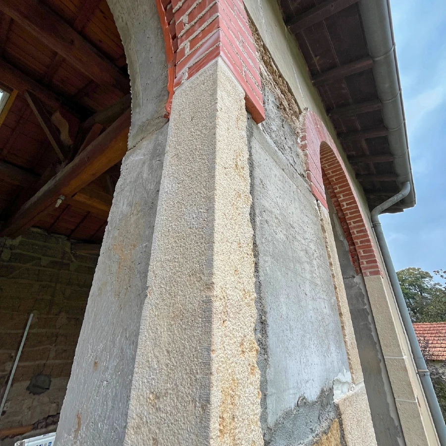 Photographie d'un chantier de rénovation structurelle montrant un mur de maison ancienne avec des fissures visible étant réparé par un maçon professionnel utilisant du mortier et des outils de maçonnerie. L'image doit montrer clairement les techniques de consolidation des structures existantes, avec des échafaudages de sécurité autour du chantier, dans une ambiance de travail professionnel et méthodique. La lumière naturelle doit mettre en évidence le savoir-faire du professionnel et la qualité de l'intervention sur un bâtiment résidentiel.