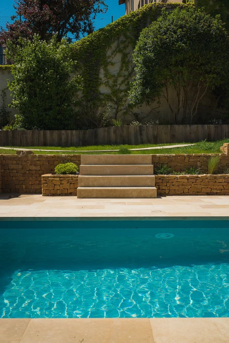 Piscine rectangulaire semi-enterrée installée sur un terrain en pente, entourée d'une végétation dense et d'un panorama boisé